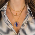 Person wearing a striped shirt and three 14k gold necklaces. One of the gold chains has three colorful fish pendants on it. 