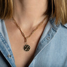 A person wearing a paperclip chain with a gold pendant attached. 