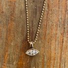 A 14k gold bezel-set marquise diamond pendant on a ball chain set on a wooden background. 