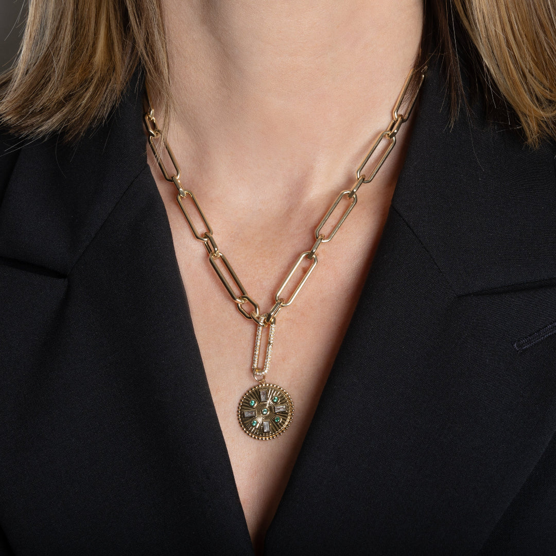 A person wearing a 14k gold chain with a diamond bail with a emerald and diamond pendant attached. 