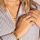 Close-up of a person wearing gold jewelry including a necklace, bracelet, and ring, with a striped shirt.