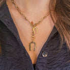 Gold necklace with two different horseshoe pendant worn by a person with a navy shirt