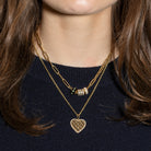 A woman wearing thin chain rolo chain with a pendant and a paperclip chain with beads against a navy sweater.
