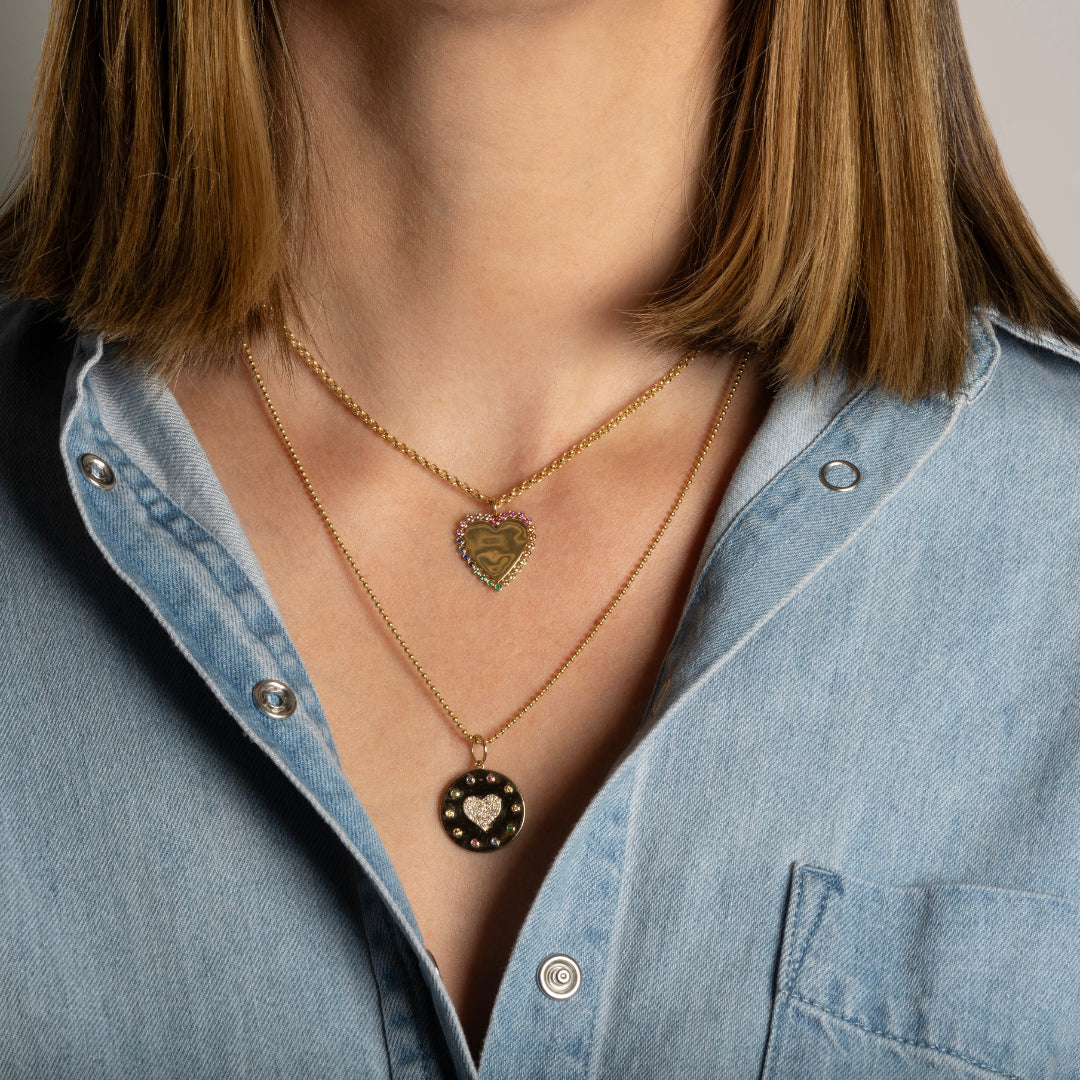 A person wearing a denim shirt layered with two 14k gold gold chains, some with charms.