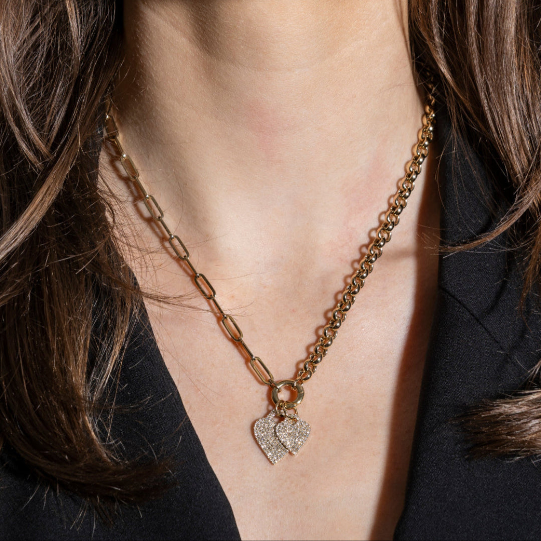 Gold chain necklace with two heart-shaped pavé diamond pendants worn by a person in a black blazer. 