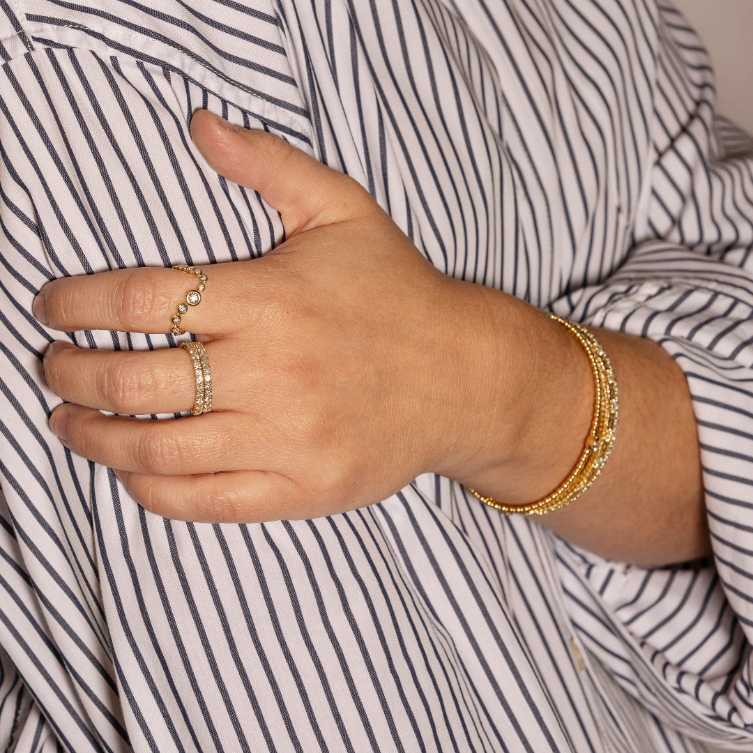 Hand wearing gold rings and bracelets against a striped shirt background