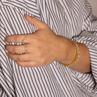Hand wearing gold rings and bracelets against a striped shirt background