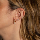 A person wearing numerous earrings with hair tucked behind her ear. 