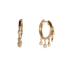 A pair of gold hoops with dangling bezel set diamonds on a white background.