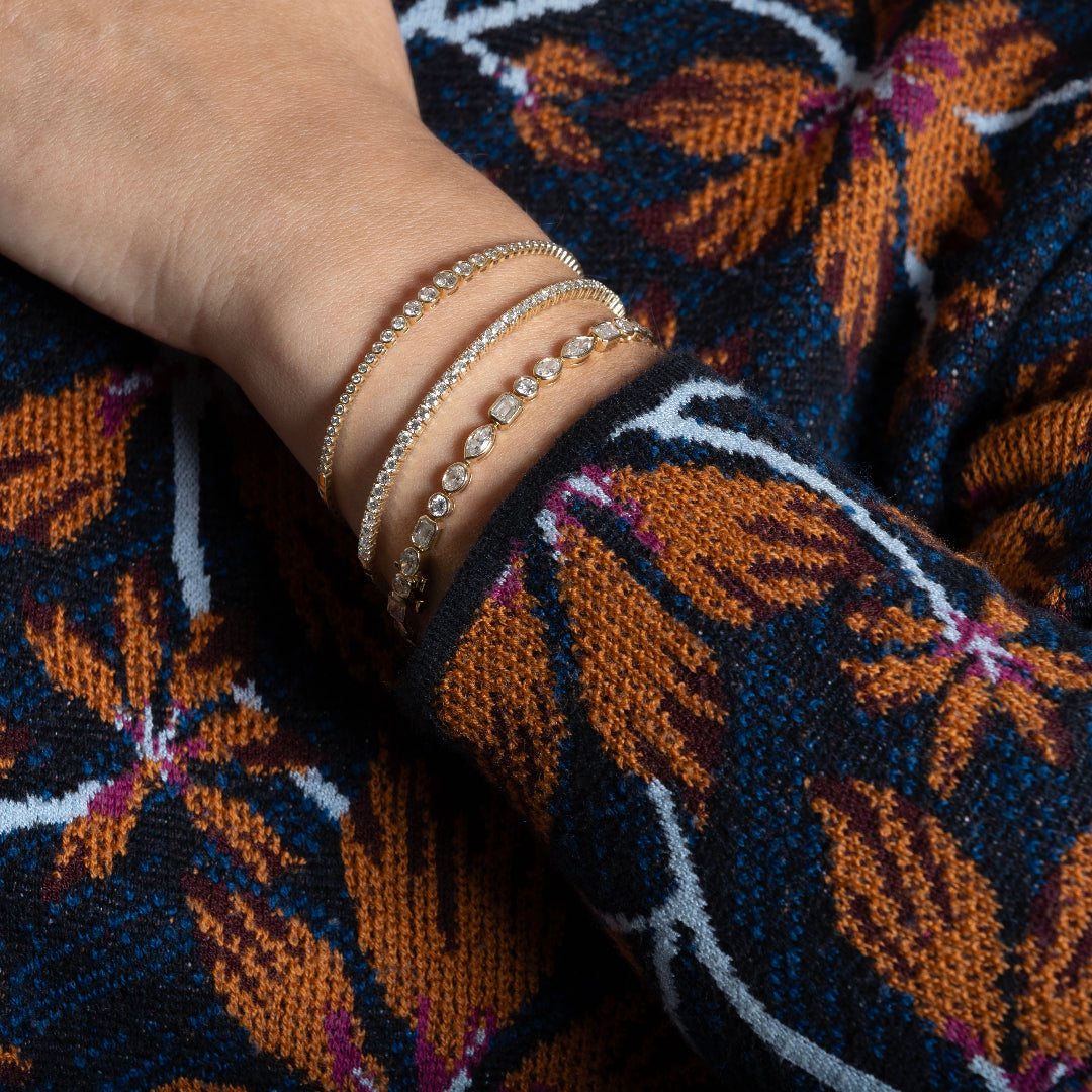 A person wearing three diamond tennis bracelets with their arm on their sweater. 