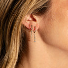 Close-up of a person wearing two pairs of dangling gold earrings with diamonds.