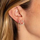 Close-up of an ear wearing two gold earrings with diamonds. 
