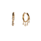 A pair of gold hoops with dangling bezel set diamonds on a white background.