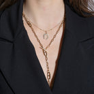 Gold chain necklace with a horseshoe pendant and a long gold lariat chain on a person wearing a black blazer.