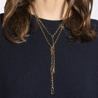 A person wearing two gold lariat chains with a navy sweater.