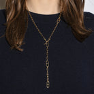 A person in a navy blue sweater wearing a gold lariat necklace. 