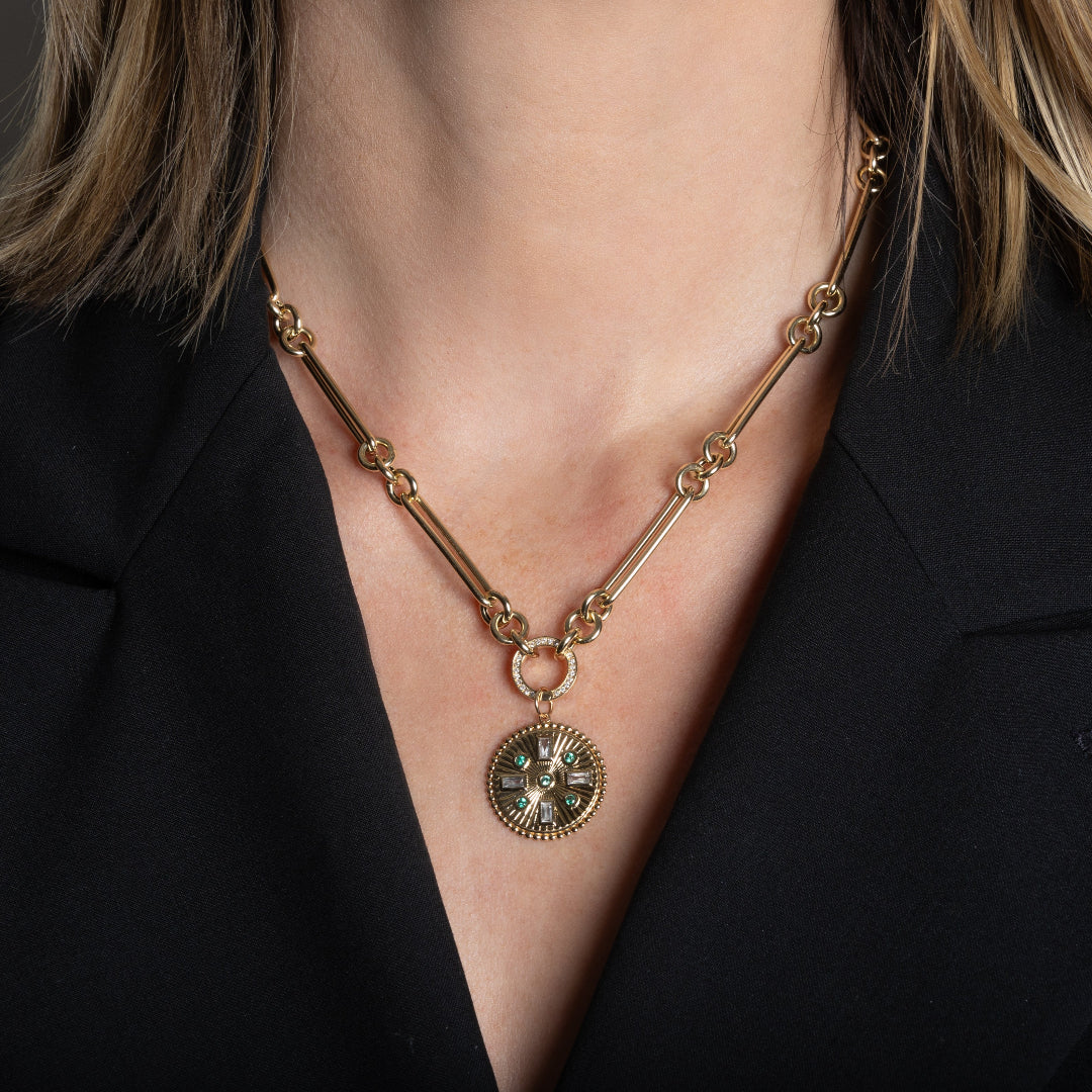 A person wearing a 14k gold necklace with a double-sided diamond enhancer, featuring oval and round link chain with a gold medallion pendant attached. 