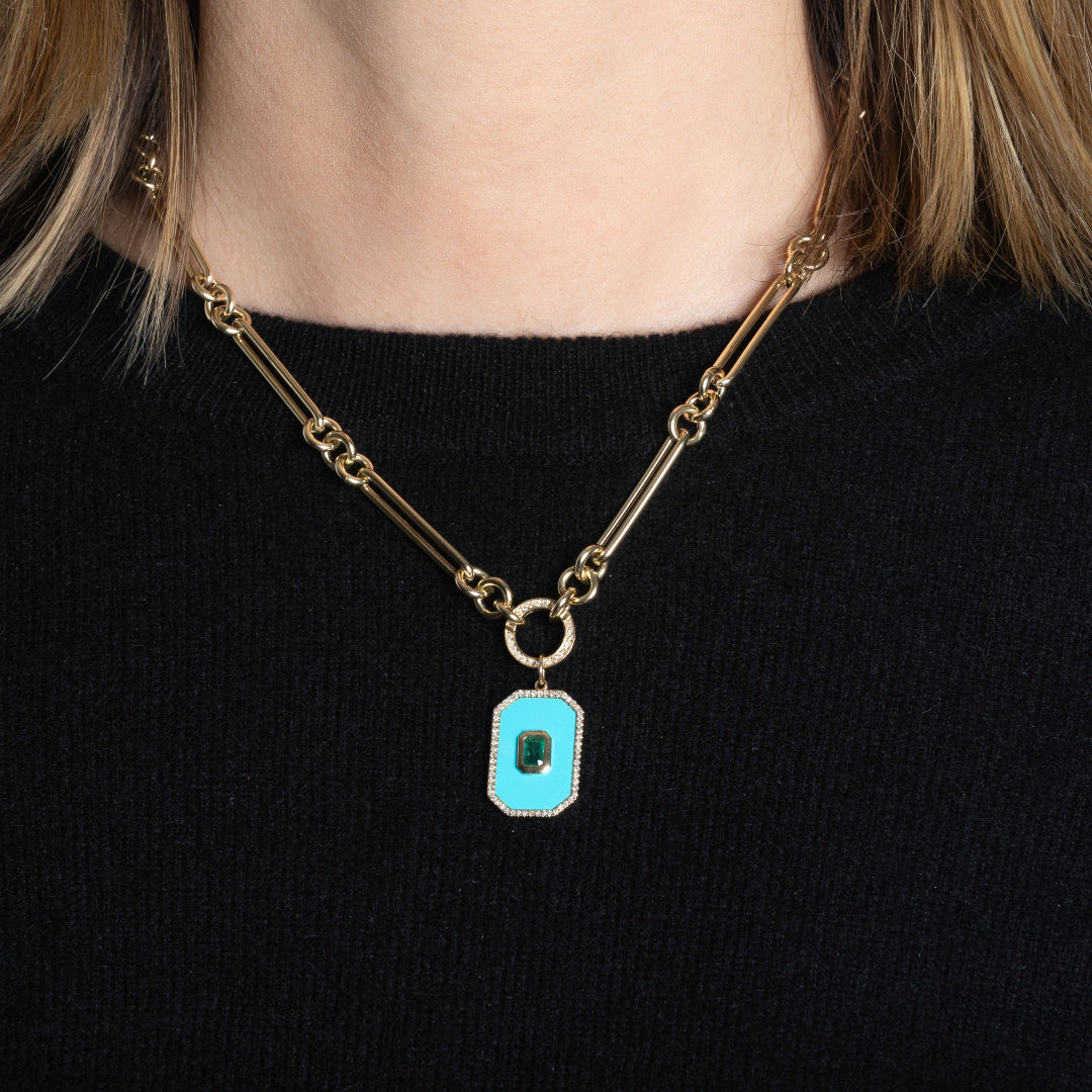 A person in a black sweater wearing a 14k gold necklace with a double-sided diamond enhancer, featuring oval and round link chains with a turquoise and emerald pendant attached. 
