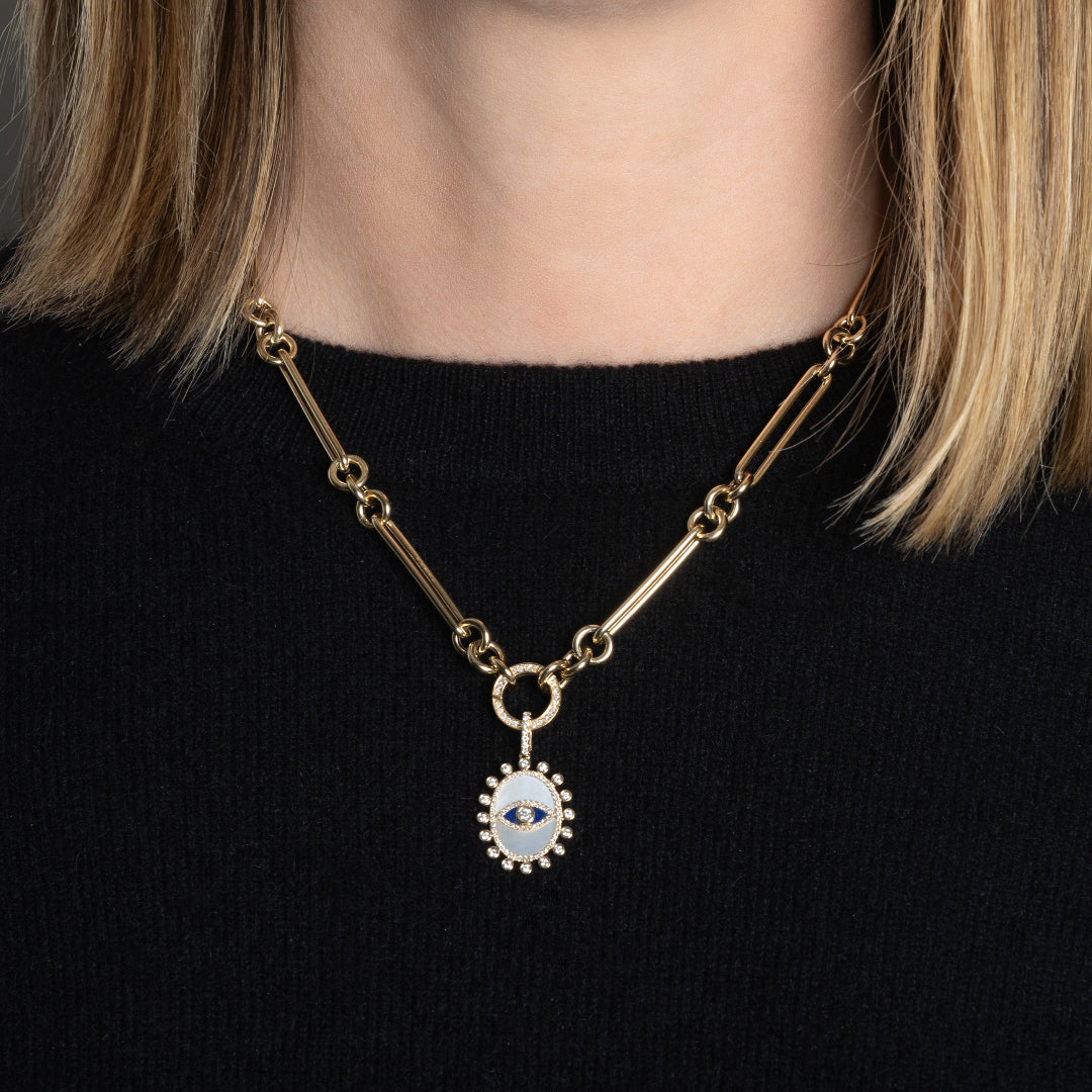 A person in a black sweater wearing a 14k gold necklace with a double-sided diamond enhancer, featuring oval and round link chains with a mother of pearl pendant attached. 