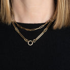 A person in a black sweater wearing a 14k gold necklace with a double-sided diamond enhancer, featuring oval and round link chains layered with a gold paperclip chain necklace. 