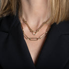 A person in a black blazer wearing a 14k gold necklace with a double-sided diamond enhancer, featuring oval and round link chains with a mixed link gold chain. 