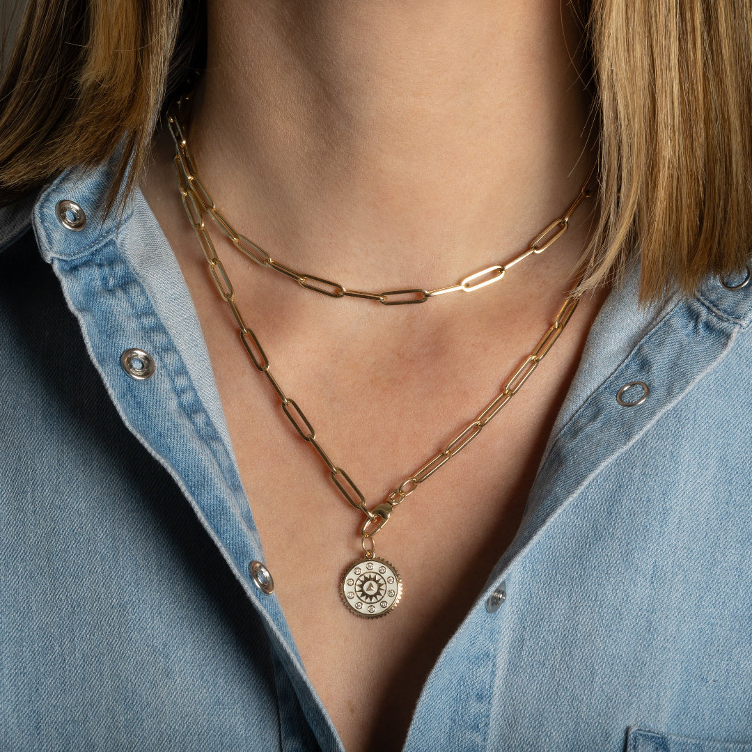Person wearing two gold paperclip chain necklaces, one with a pendant. 