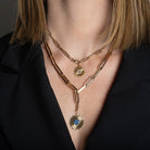 A person wearing two paperclip chain necklaces; one chain has a gold and diamond starburst pendant and the other chain is chunkier and styled lariat-style with a circle pendant featuring a blue sapphire heart.