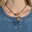 A person wearing a 14k gold paperclip chain necklace with three diamond and gold roundel beads and a black enamel and emerald roundel bead. 