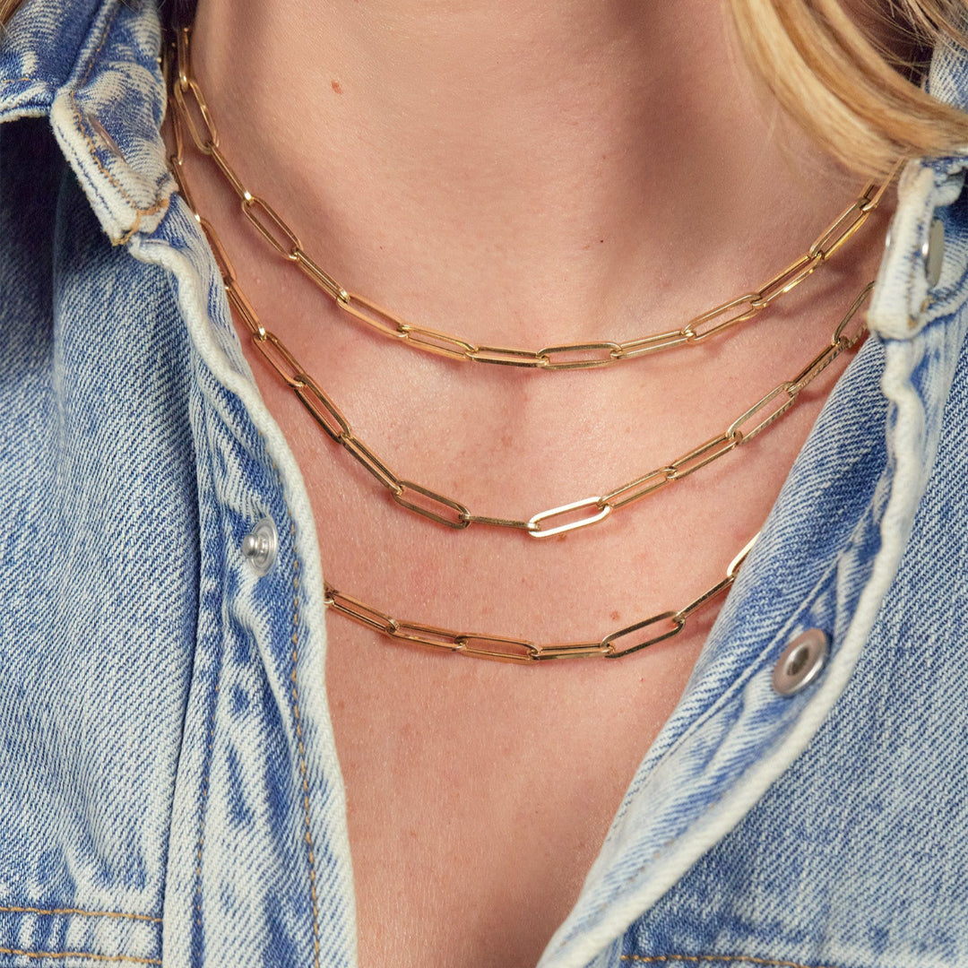 Two 14k gold paperclip chain necklaces layered on a person wearing a denim jacket.