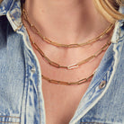 Two 14k gold paperclip chain necklaces layered on a person wearing a denim jacket.