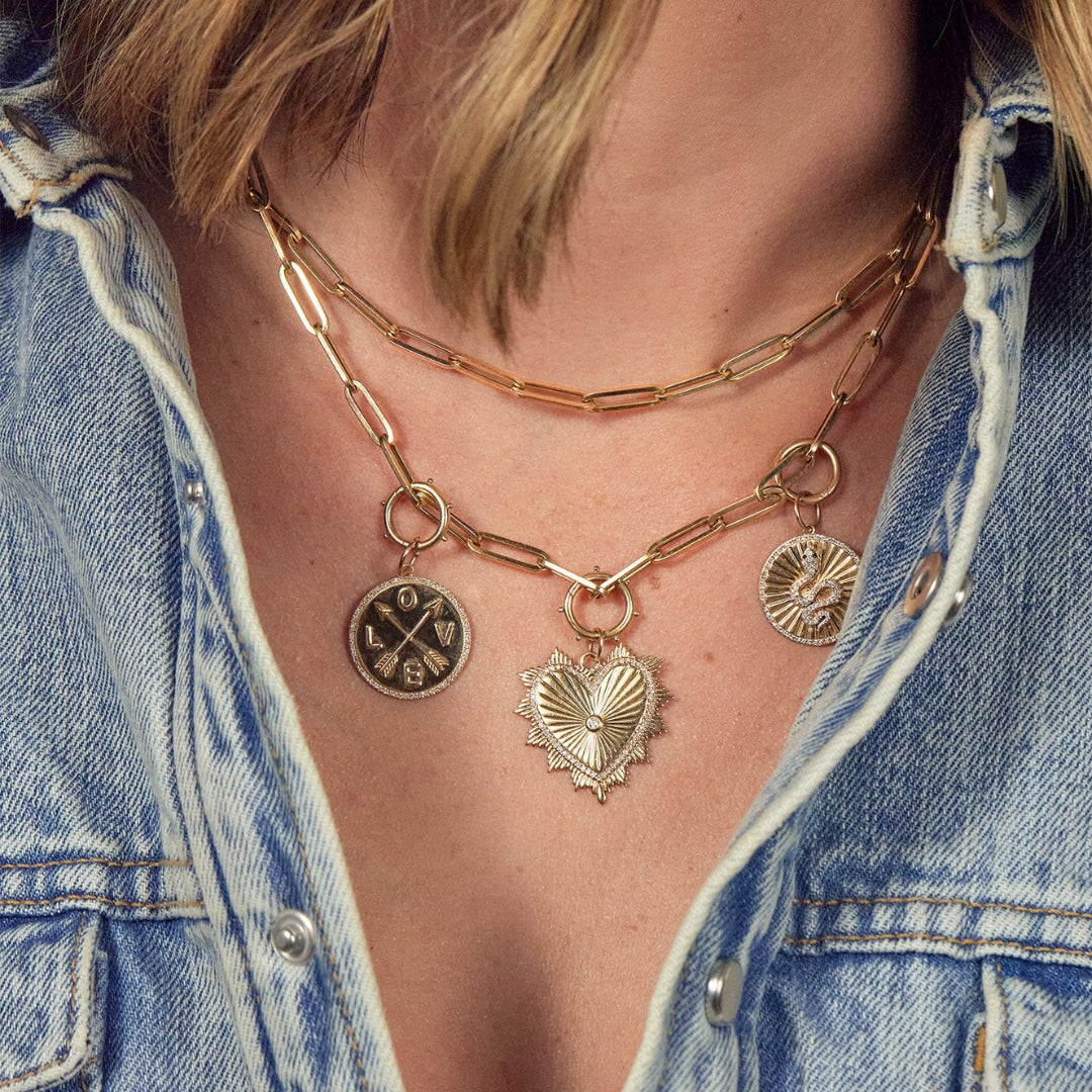 A person wearing two layered 14k paperclip chain necklaces, one adorned with charms.