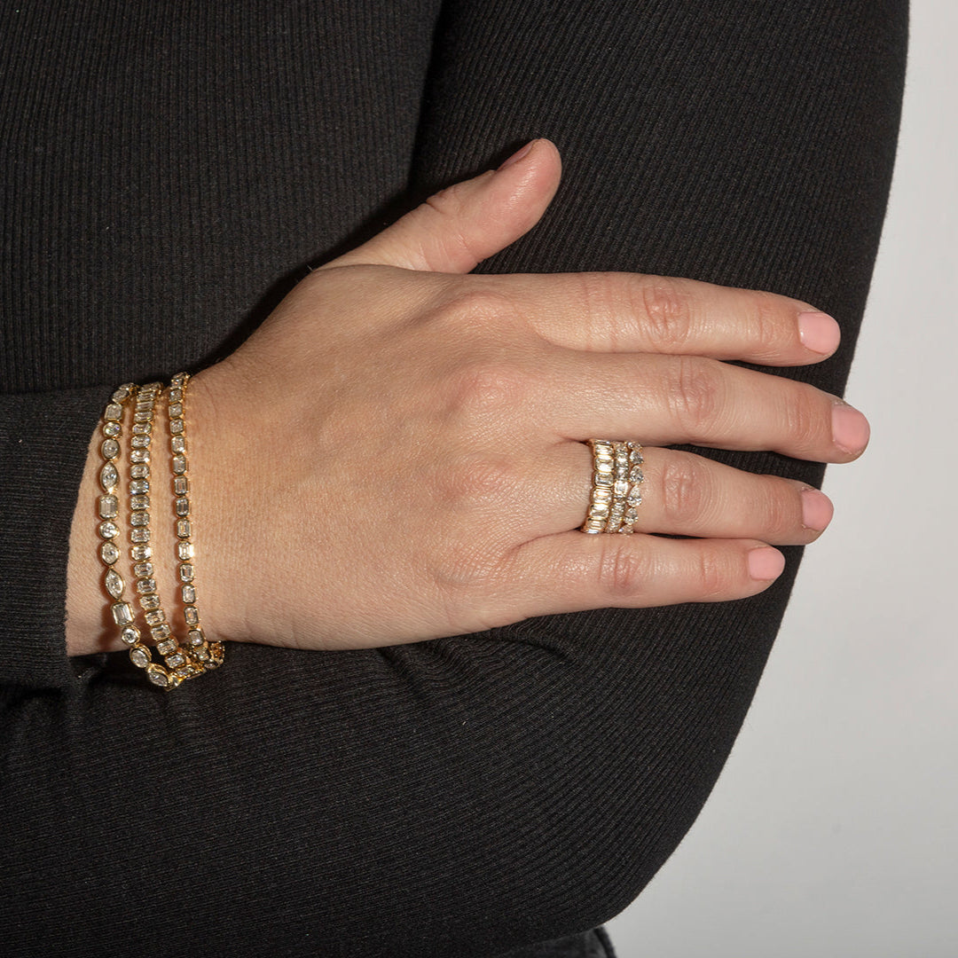 A person wearing three diamond tennis bracelets and three diamond stacking rings. 