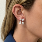 A close up of a women's ear with two pear drop earrings and wearing a blue blazer. 