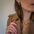 A person wearing a trenchcoat and three 14k gold necklaces. 