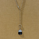 A 14k gold rolo chain with a onyx and diamond scarab pendant on a yellow textured background.