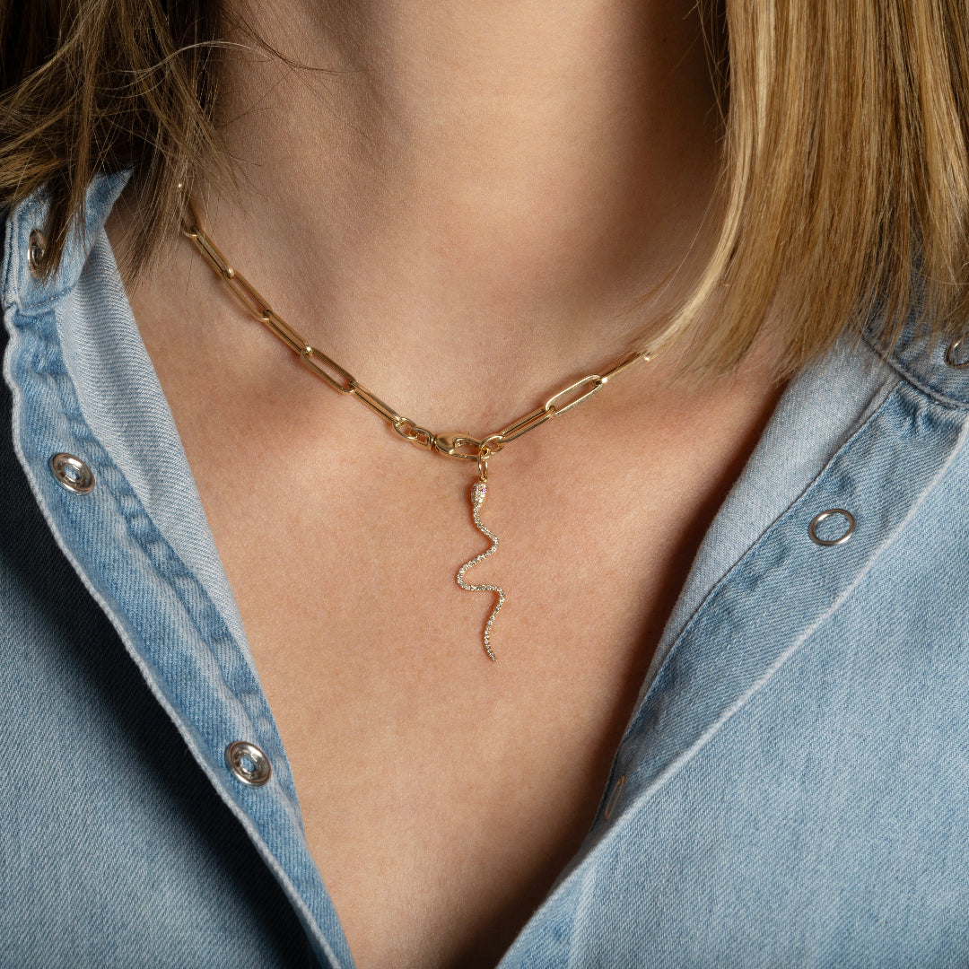 A person wearing a gold paperclip chain chain with a diamond serpent pendant. 