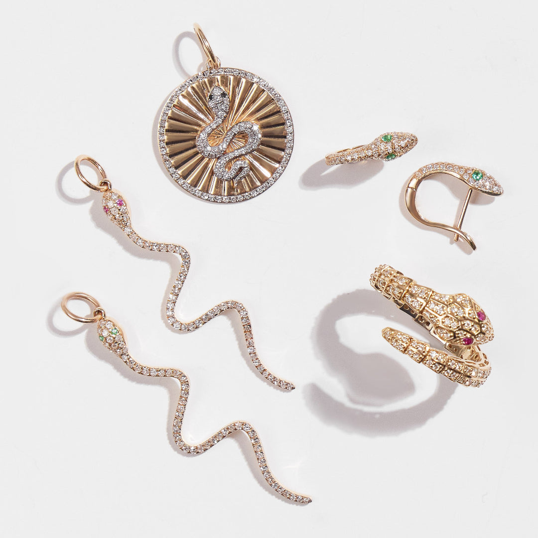 A collection of jewelry all featuring serpents; all gold with diamonds. There are two serpent diamond pendants, a serpent diamond medallion, serpent huggie earrings and a flexi ring. 