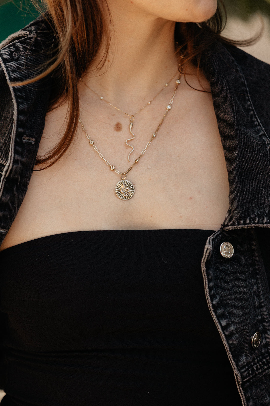Person wearing a delicate necklace with a circular pendant, with a blurred background.