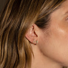 Close-up of a person wearing gold diamond serpent earrings with a neutral background.