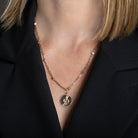 A person wearing a 14k gold diamond station paperclip necklace with a gold and diamond serpent pendant attached. 