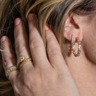 Someone swiping their hair back while wearing two 14k gold and diamond rings. 
