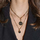 Layered gold necklaces with a black pendant on a person wearing a black top.