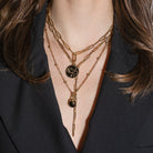 Close-up of a person wearing multiple gold necklaces with serpent pendants and a black blazer. 