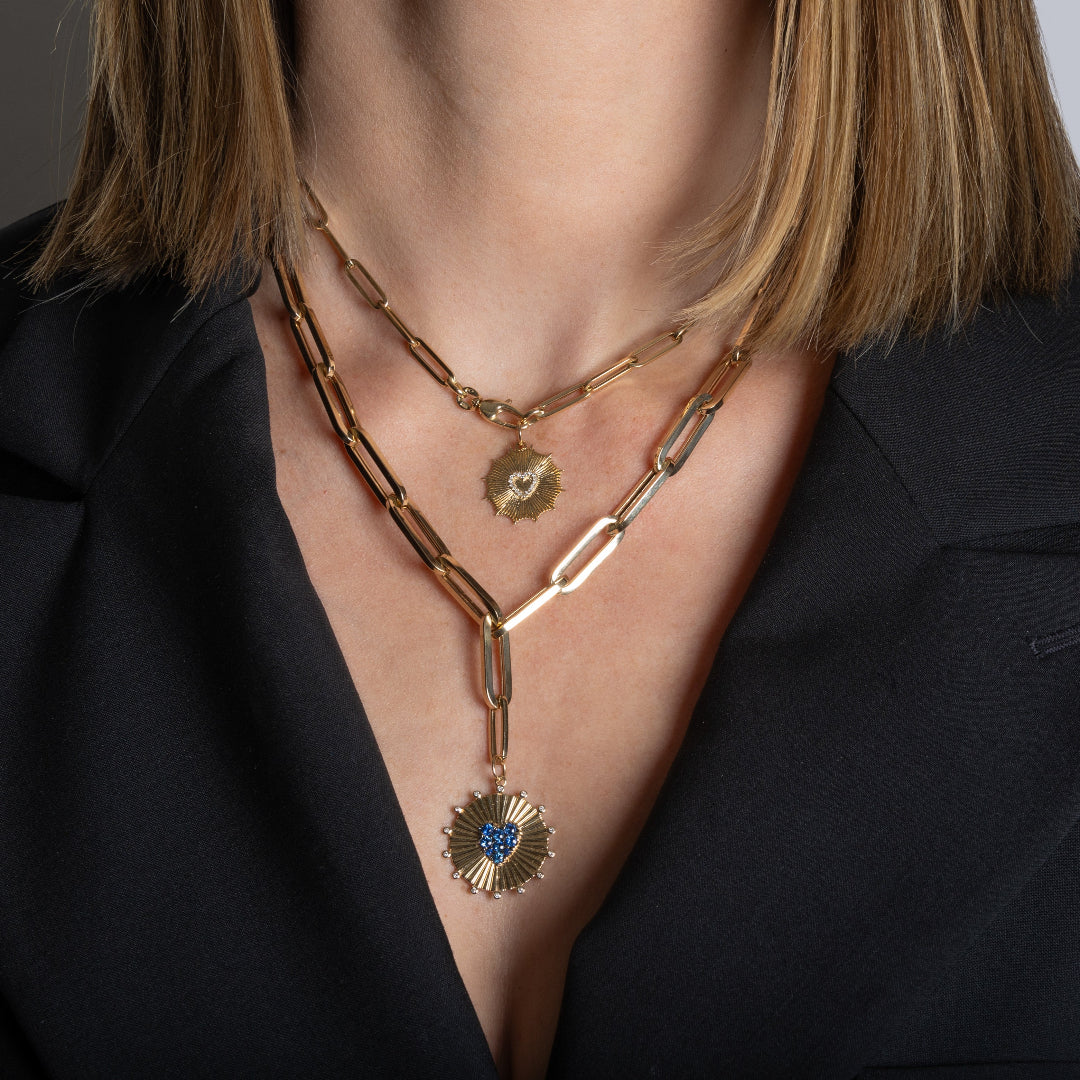 A person wearing two chunky paperclip chain necklaces, both with gold pendants. 