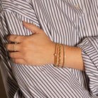 Hand wearing gold bracelets and rings with a striped shirt background