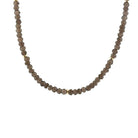 A beaded necklace made of small faceted smoky quartz beads with a few small gold spacer beads, shown against a plain white background.