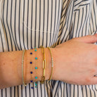 Close-up of a person wearing a striped shirt and her wrist wearing multiple 14k gold bangles with diamonds and beaded stone bracelets with turquoise and lapis.