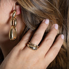 A person pulling their hair back to showcase gold three link diamond earrings and two gold rings. 