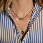 Necklaces with lapis, turqoise and diamond pendants and gold chains on a person wearing a striped shirt.