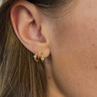 Close-up of an ear wearing 14k gold huggie earrings with small diamonds.